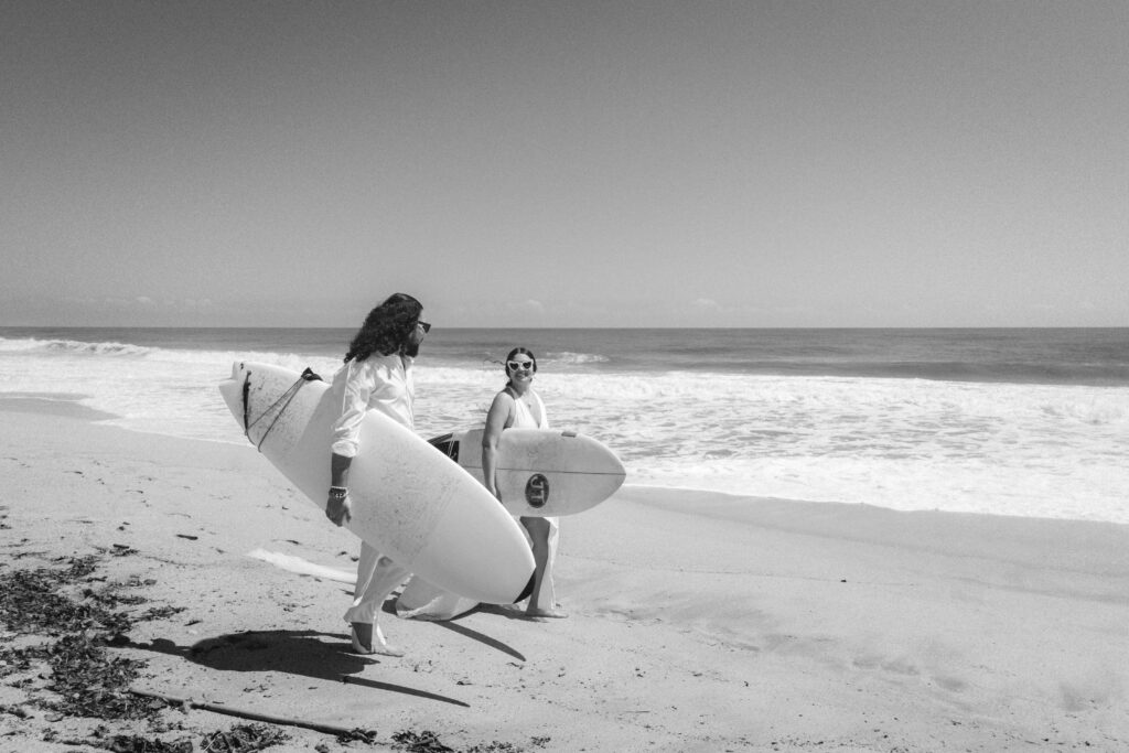 The couple beams with joy as they stand by the ocean, surfboards ready, celebrating their union with a tropical twist in Parque Tayrona, Colombia. Captured by Jan Schick.  – Das Paar strahlt vor Freude am Ozean, die Surfbretter bereit, und feiert ihre Hochzeit mit einem tropischen Touch im Parque Tayrona, Kolumbien. Festgehalten von Jan Schick.