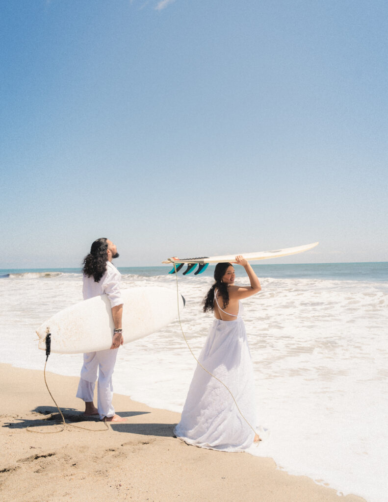 The bride and groom carrying surfboards along the Colombian coastline, blending romance and adventure in Tayrona National Park.  Braut und Bräutigam tragen Surfbretter entlang der kolumbianischen Küste und vereinen Romantik und Abenteuer im Tayrona-Nationalpark.