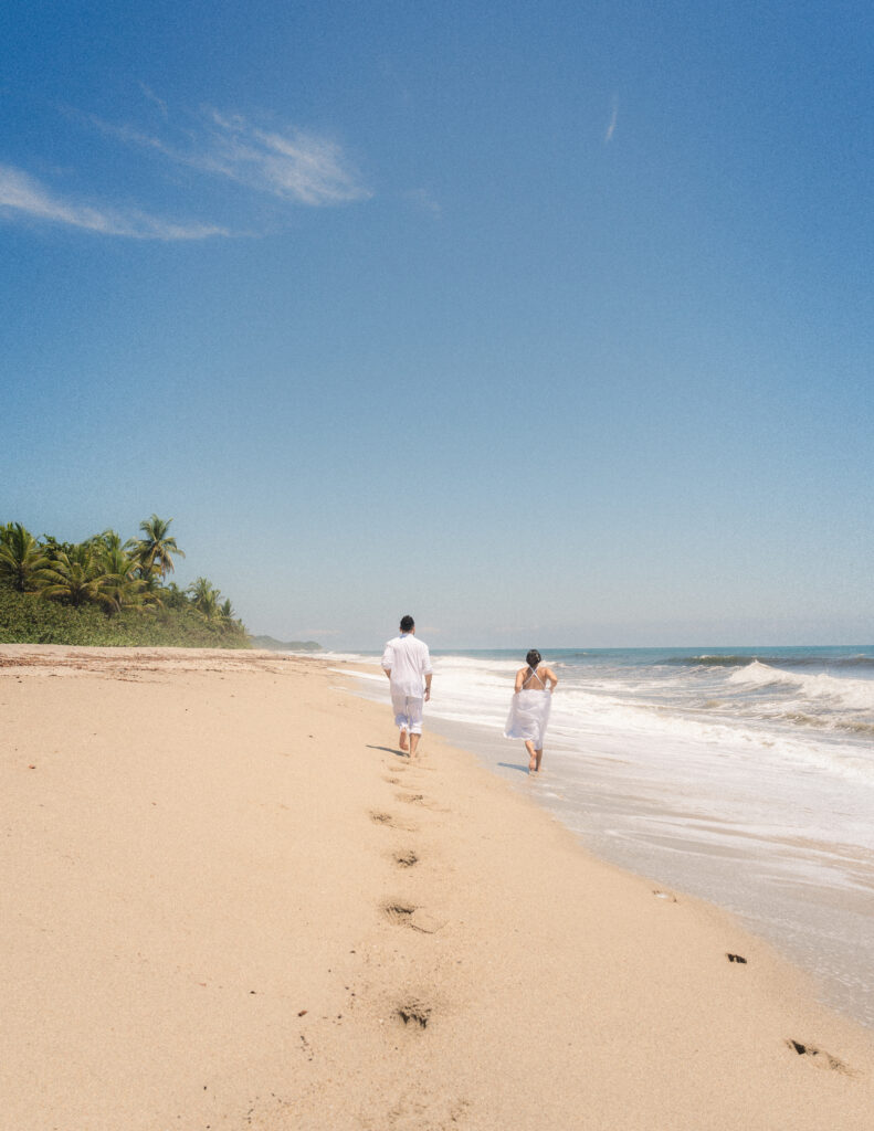 The bride and groom leave footprints on the golden sand as they walk together on the scenic beaches of Tayrona National Park. Braut und Bräutigam hinterlassen Fußspuren im goldenen Sand, während sie gemeinsam die malerischen Strände des Tayrona-Nationalparks erkunden.