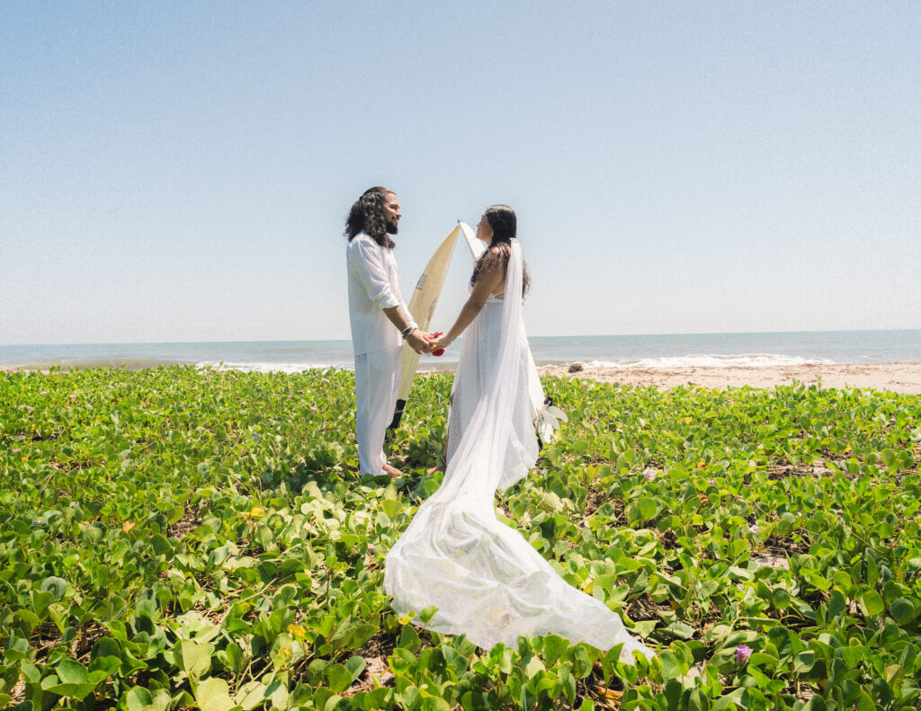 The couple stands amidst vibrant greenery and ocean waves, exchanging vows in an intimate elopement ceremony at Parque Tayrona, Colombia. Captured by Jan Schick Photography. – Das Paar steht inmitten lebhafter Grünflächen und Meereswellen und tauscht Gelübde in einer intimen Elopement-Zeremonie im Parque Tayrona, Kolumbien, aus. Festgehalten von Jan Schick Photography.