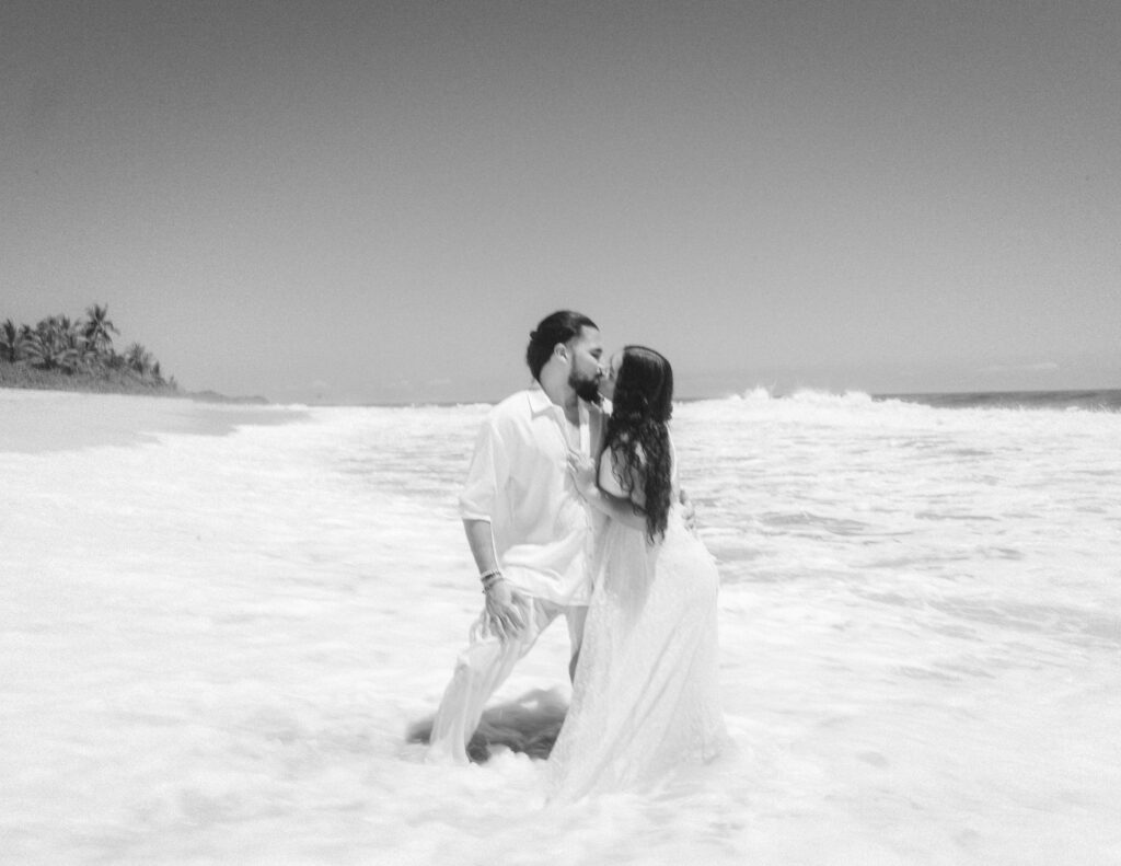 The couple shares a romantic kiss in the waves of the ocean during their elopement in Tayrona National Park, Colombia. Das Paar teilt einen romantischen Kuss in den Wellen des Ozeans während ihres Elopements im Tayrona-Nationalpark in Kolumbien.