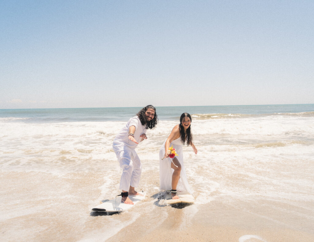 The couple playfully pretends to surf together during their elopement, celebrating love and fun on the beach in Tayrona. Das Paar tut spielerisch so, als würde es surfen, und feiert Liebe und Spaß während ihrer Elopement-Hochzeit am Strand von Tayrona.